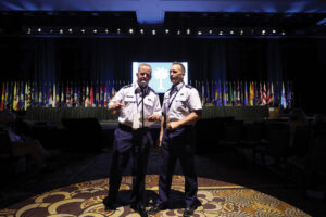 Two men dressed in uniform giving presentation spotlit on a dark stage.