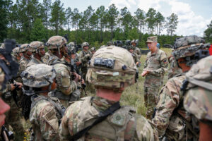 Soldiers huddled around and standing in a field in combat gear